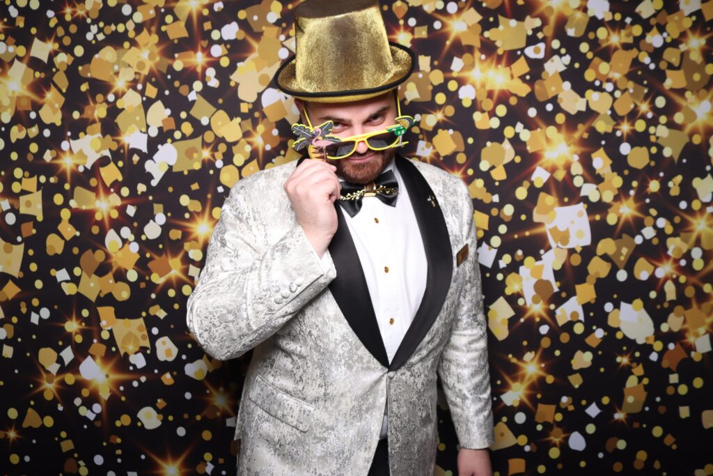 Nathan Cassar, Wedding & Corporate Master of Ceremony in gold top hat at party backdrop