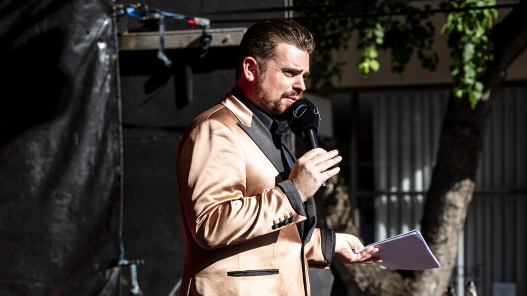 Man in gold blazer speaking into microphone outdoors