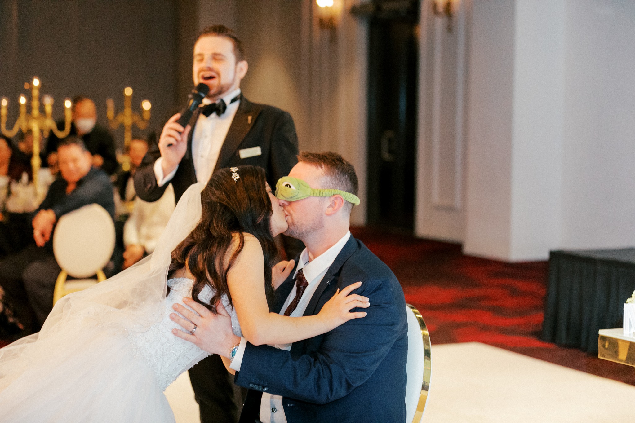 Bride kissing blindfolded groom at wedding reception game