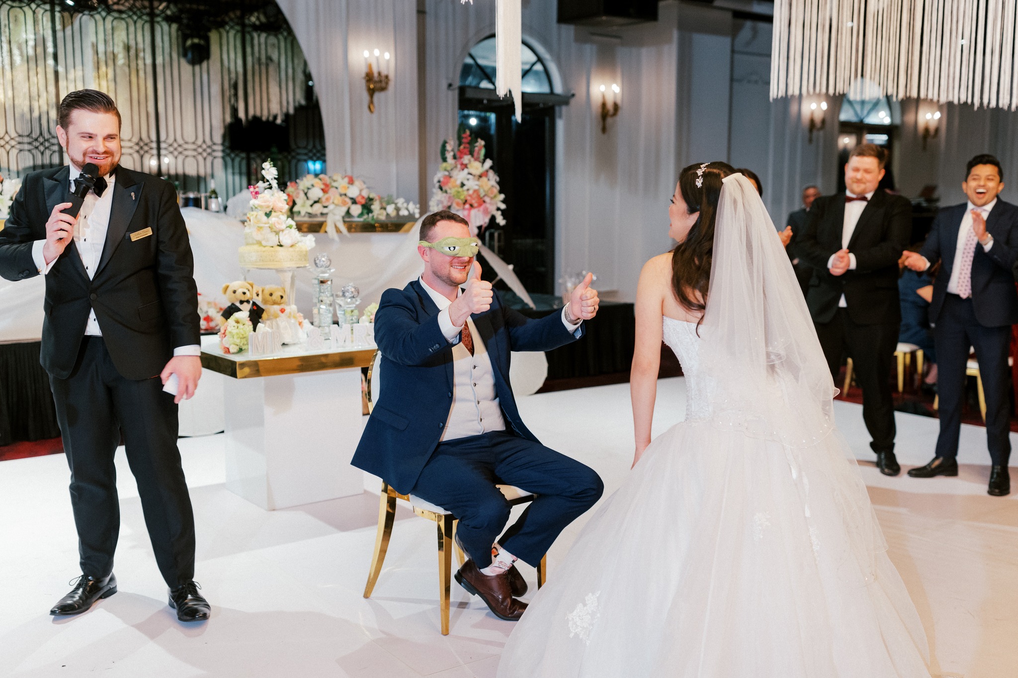 Groom blindfolded during wedding reception game with bride