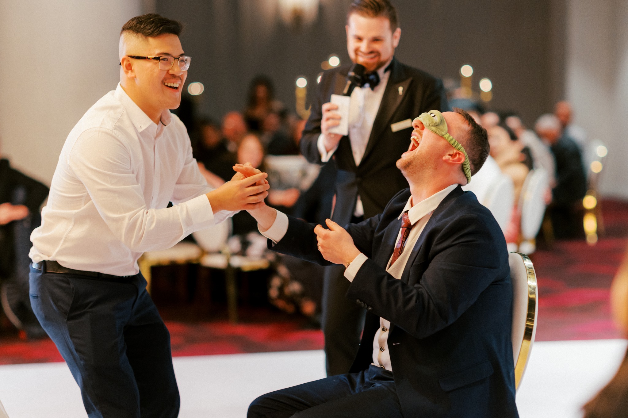 Groom blindfolded laughing during wedding reception game