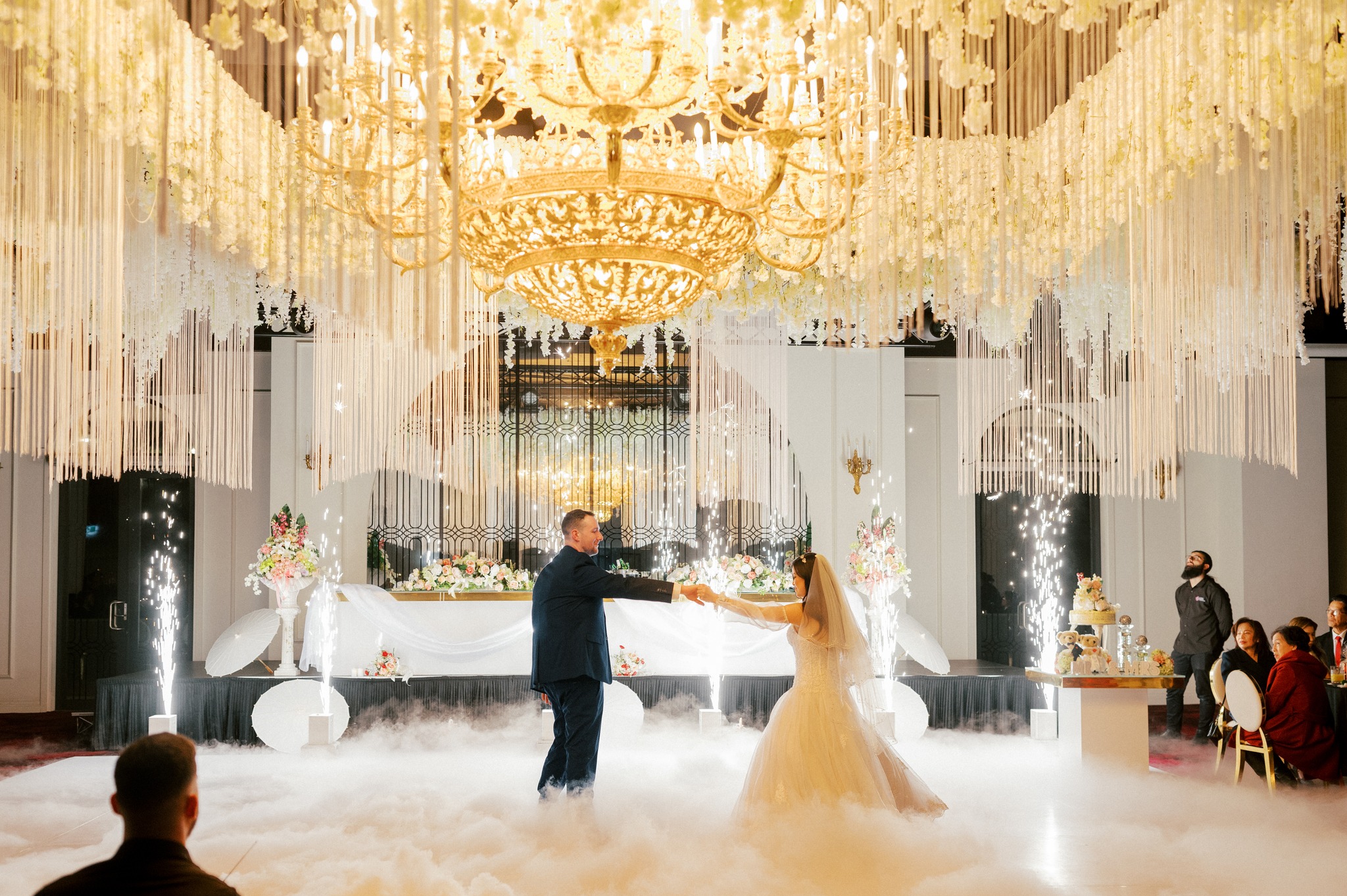 Bride and groom dancing beneath chandelier and sparklers