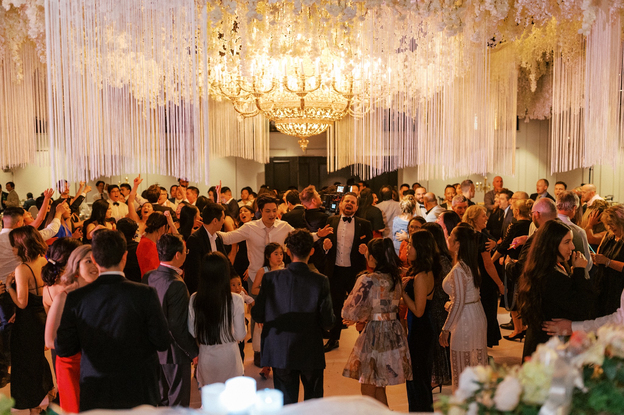 Guests dancing beneath chandelier at elegant wedding reception